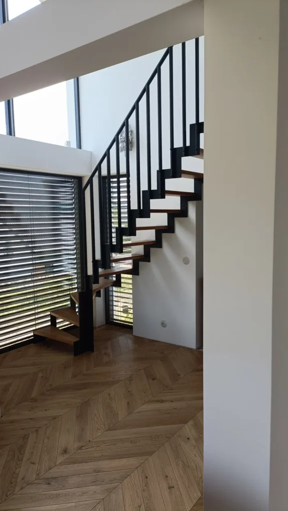 Nowoczesne schody z czarną balustradą w wykończonym domu pod klucz w Sławkowicach pod Krakowem.